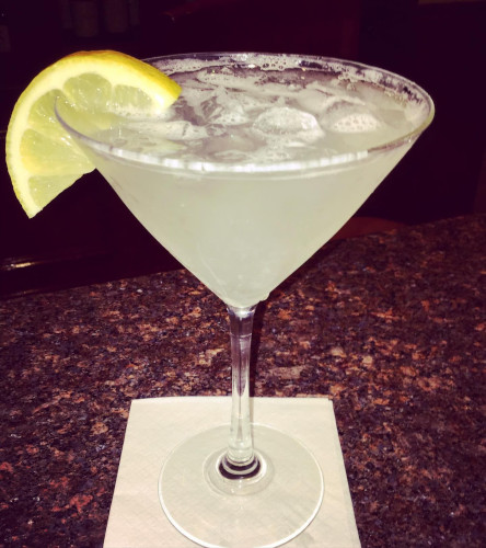 Lemon drop martini with a lemon wedge on a napkin atop a granite bar