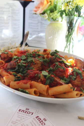 Rigatoni with meatballs, tomato sauce and fresh basil beside a vase of flowers