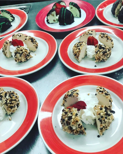 Red-rimmed plates of nut-crusted ice cream desserts with whipped cream and strawberry