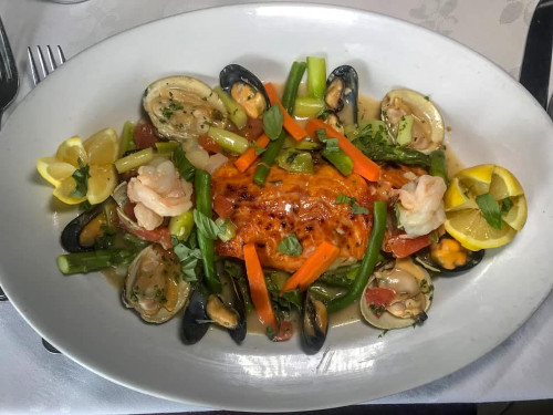 Salmon topped with seafood on a platter with mussels, clams, shrimp, carrots and lemon