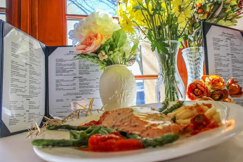 Salmon with asparagus and tomato beside penne, with menus and flowers behind