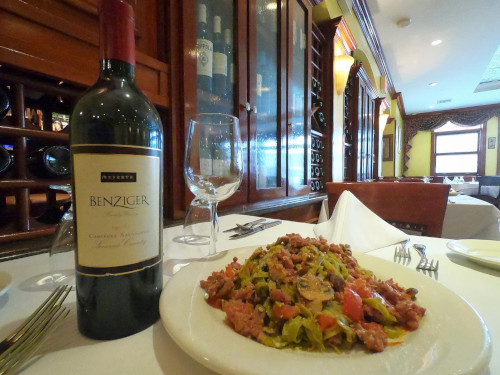 Plate of sausage and greens beside a Benziger Cabernet bottle in the dining room