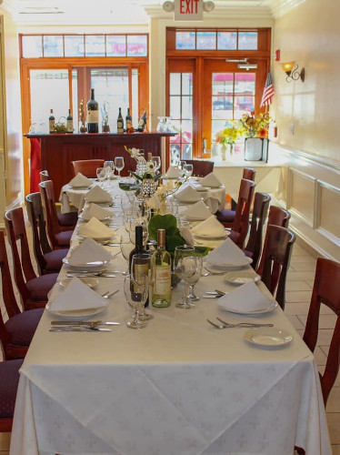 Long banquet table set with napkins, wine and flowers, wood bar beyond