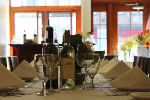 Banquet table set with folded napkins, wine glasses and bottles near sunlit windows