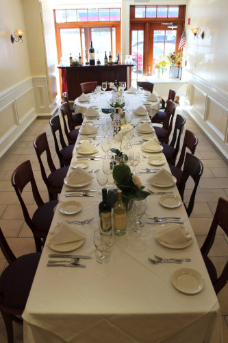 Long narrow table set for a party, with wine bottles and burgundy-cushioned chairs