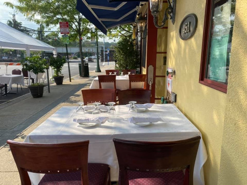 Enzo's sidewalk patio table set with white linens beneath a blue awning