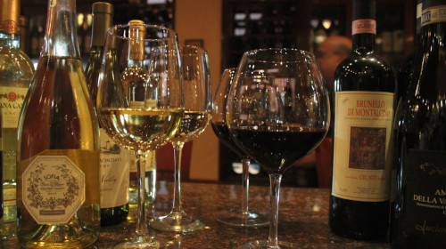Glasses of white and red wine beside Brunello and sparkling wine bottles
