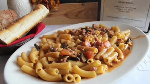 Rigatoni with sausage, eggplant and tomato sauce, with bread basket and menu behind
